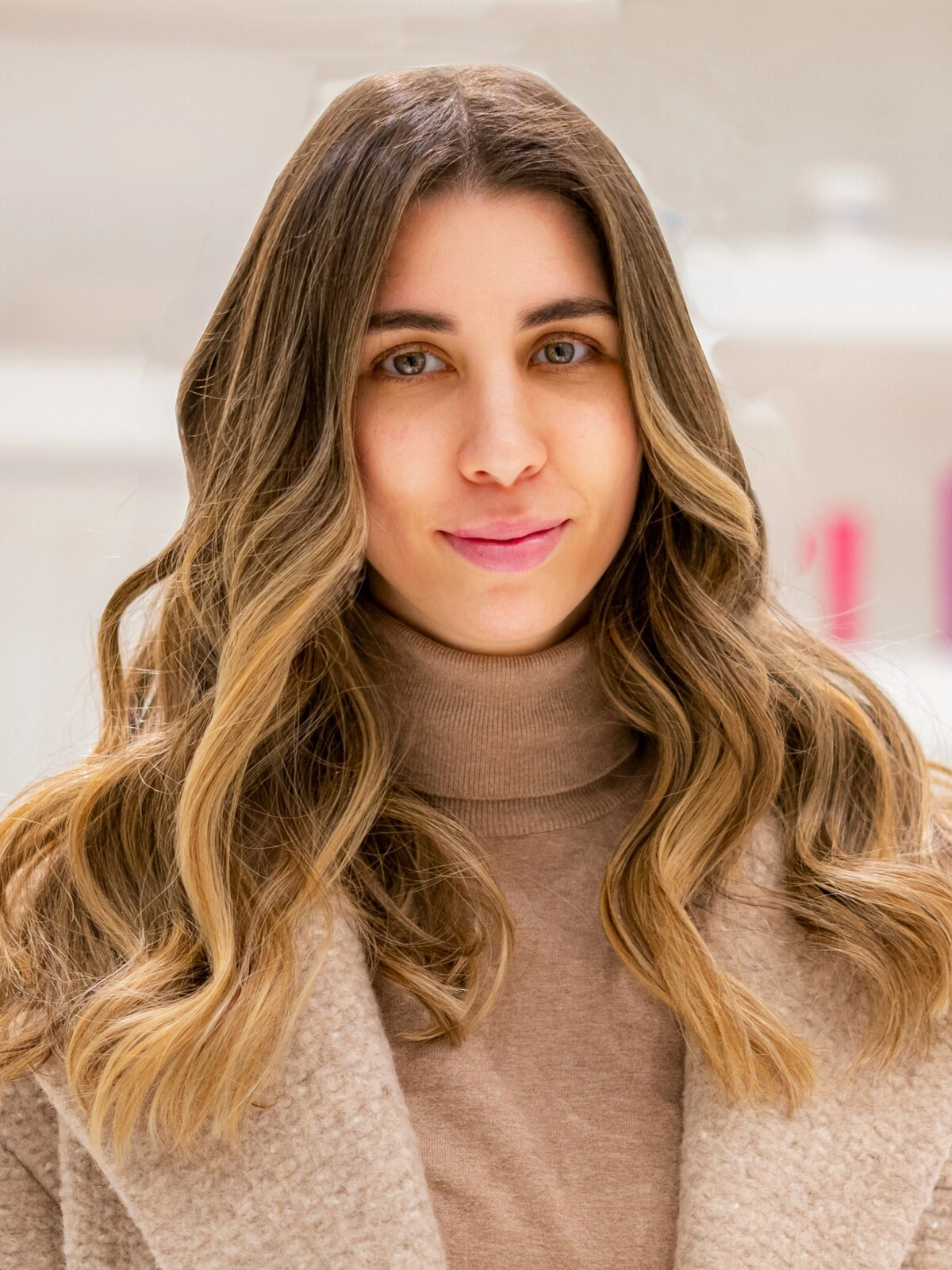 Une femme en col roulé et manteau de laine couleur camel, avec un balayage souple et ondulé où le brun se fond dans des tons caramel