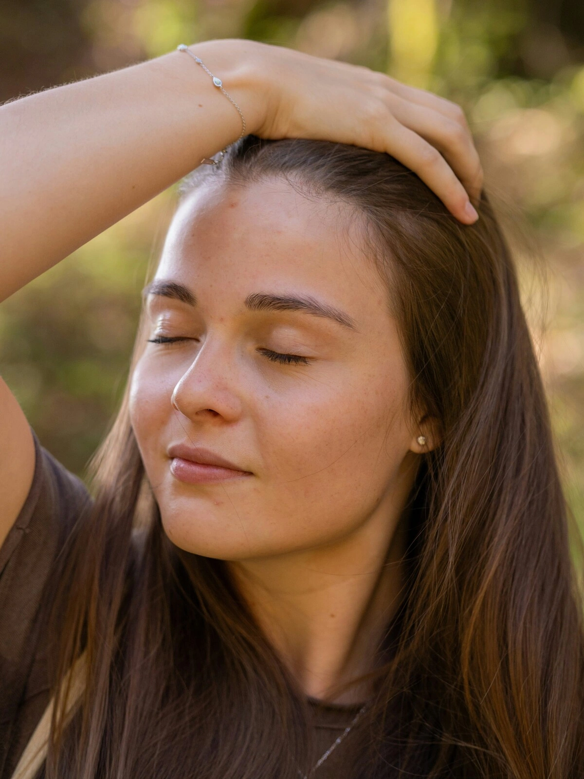 Une femme aux yeux fermés et à l'air détendu passe la main sur sa tête et dans ses longs cheveux châtains