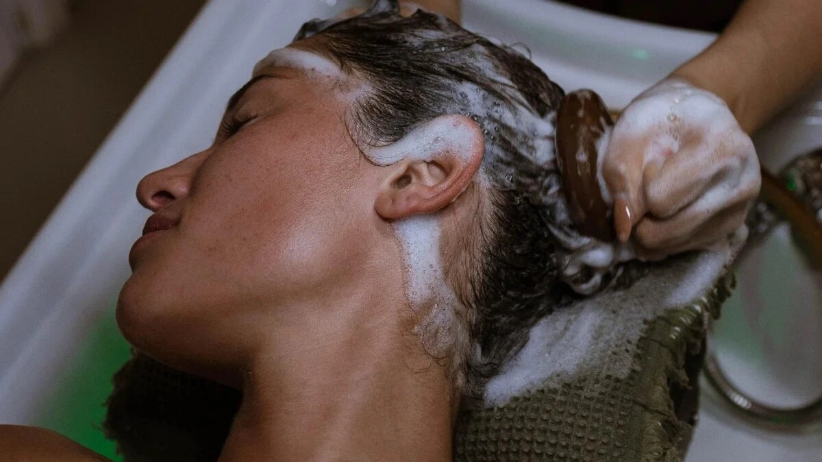 Gros plan d'un praticien réalisant un head spa japonais avec une brosse pour cuir chevelu sur une cliente