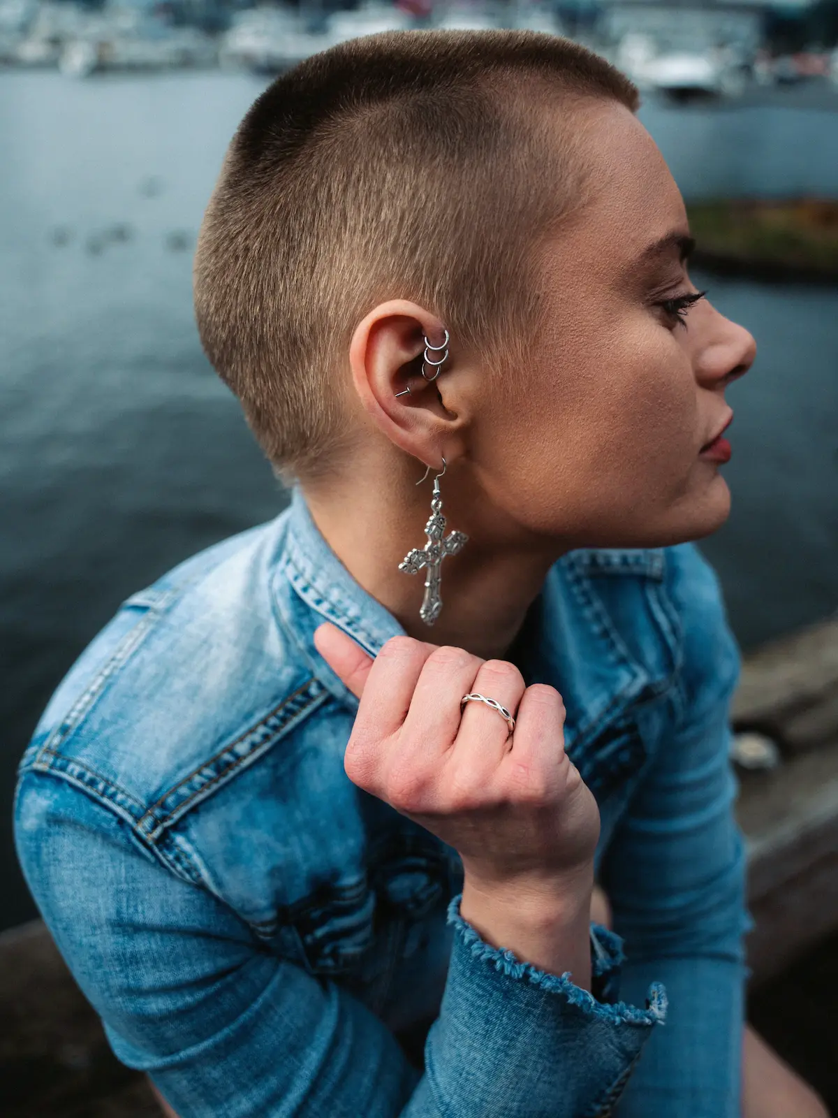 Vue en plongée d'une femme portant des piercings forward helix, hélix et lobe, assise au bord d'une rivière en ville