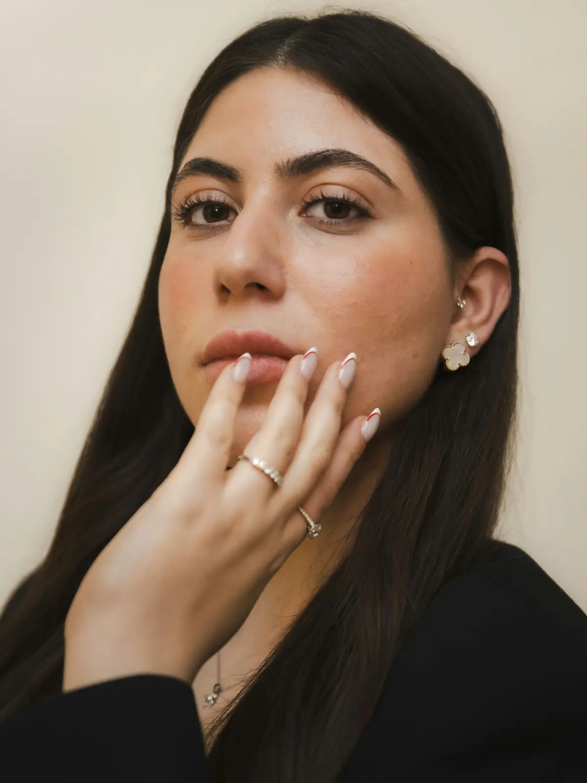 Photo en studio d'une femme portant des piercings au lobe et au tragus, une main manucurée posée sur le visage