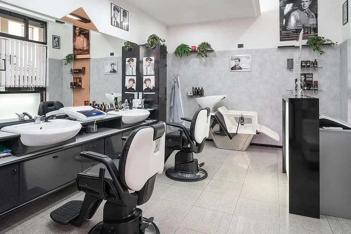 Fauteuils de barbier vintage et bacs à shampoing chez Fabio Desole Acconciature Maschili à Sassari, avec portraits encadrés au mur.