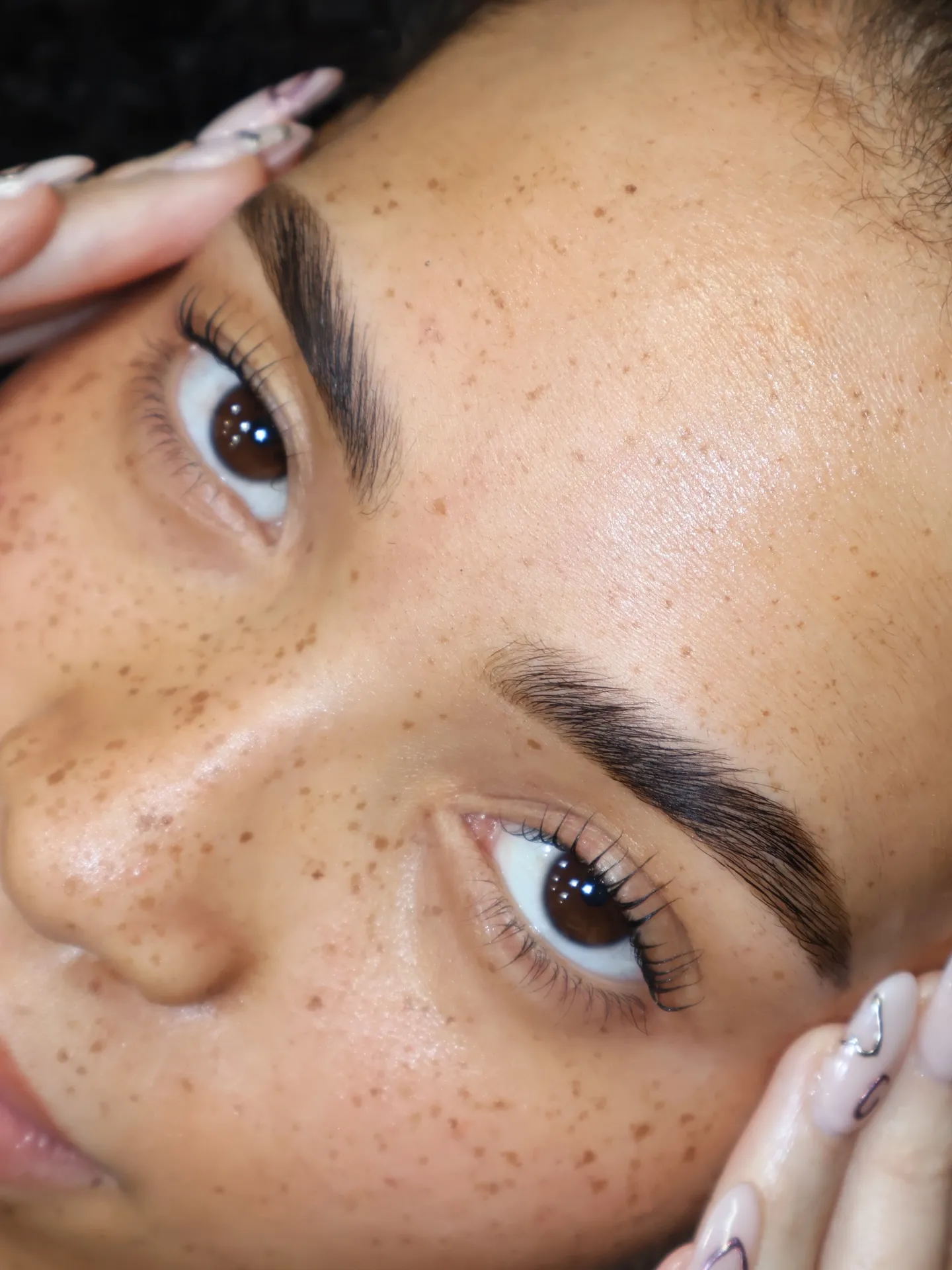 Gros plan sur des cils naturellement rehaussés après un rehaussement de cils coréen, courbe douce et bien séparée à la texture aérienne, sur une peau constellée de taches de rousseur