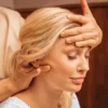 Gros plan sur une femme aux yeux fermés pendant un massage indien de la tête, une praticienne posant une main sur son front et massant sa nuque de l'autre