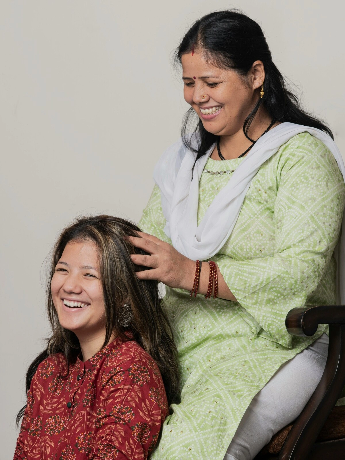 Une femme indienne en tenue traditionnelle, assise sur une chaise en bois, pratique un massage indien de la tête sur une femme assise au sol