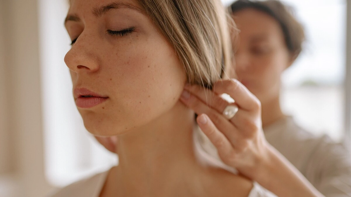 Gros plan sur une femme aux yeux fermés pendant un massage indien de la tête, une praticienne appuyant des deux mains sur la base de son crâne